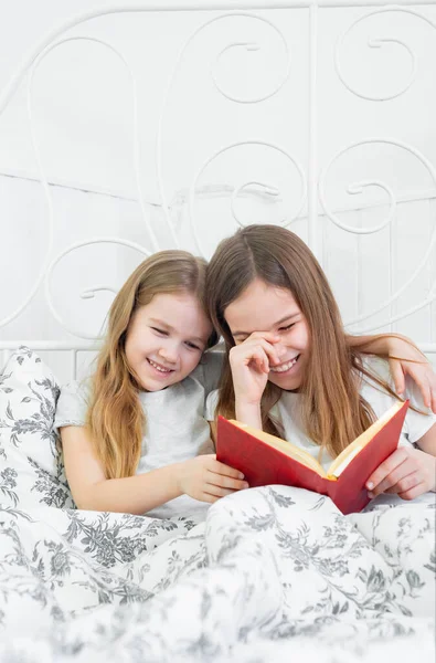 girls reading a funny book together sitting in bed