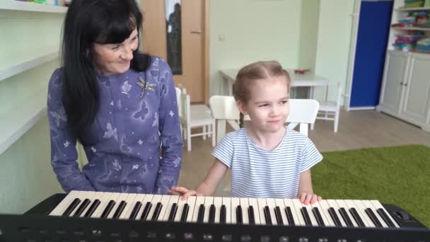 Vrouw leert klein meisje om te spelen op synthesizer — Stockvideo