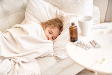 Küçük kız kanepede yatıyor ve hasta. Soğuk algınlığına iyi gelir..