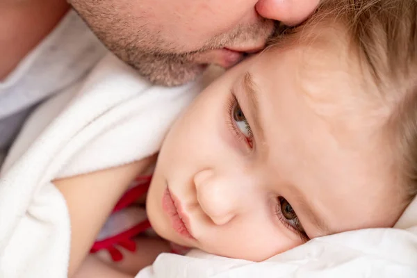 Dad kisses little sick daughter sleeping on bed. — Stock Photo, Image