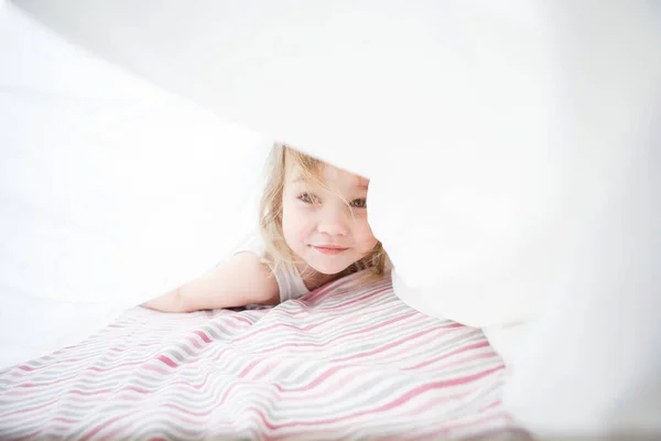 Niña jugando debajo de la manta en la cama . — Foto de Stock