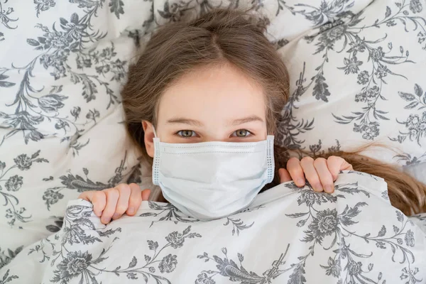 Egy tini lány fekszik az ágyban orvosi maszkban. felülnézet — Stock Fotó
