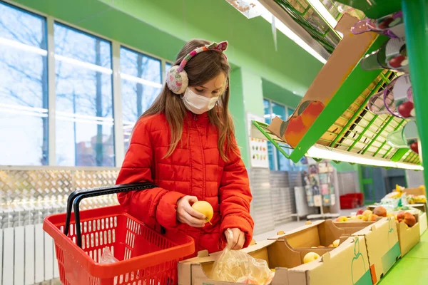 girl in mask in store picks fruit vegetables.