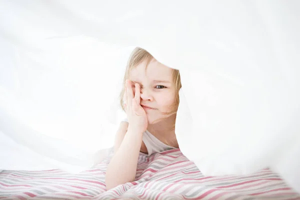 Piccola ragazza che gioca sotto coperta sul letto . — Foto Stock