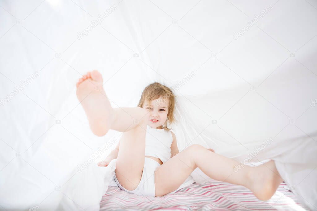 little girl playing under blanket on bed.