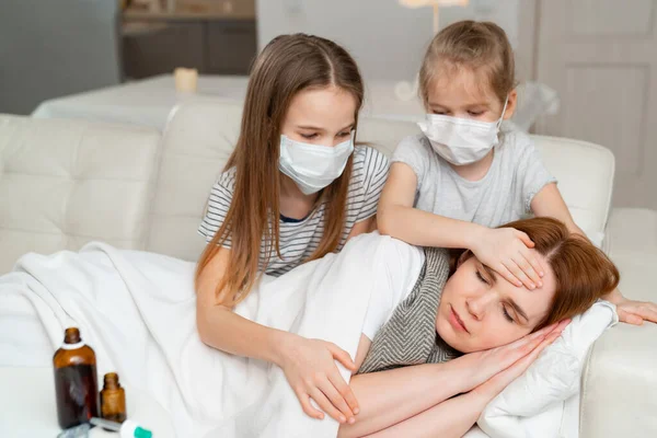 Los niños en las máscaras toman la temperatura de la madre enferma . — Foto de Stock