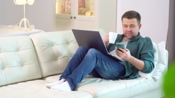 Homem bebe chá, verifica e-mail no telefone, trabalha em casa . — Vídeo de Stock