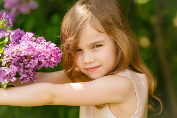 Niña pequeña en cerca de una flores de color lila con ramo — Foto de Stock