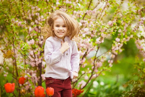 Engraçada menina perto com amêndoa arbusto e tulipas — Fotografia de Stock