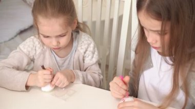 Kız kardeşler paskalya yumurtalarına yiyecek işaretleri çizerler..