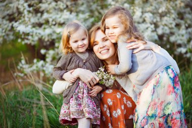 Anne ve kızları çiçekli çalılıklarda oturuyorlar. 