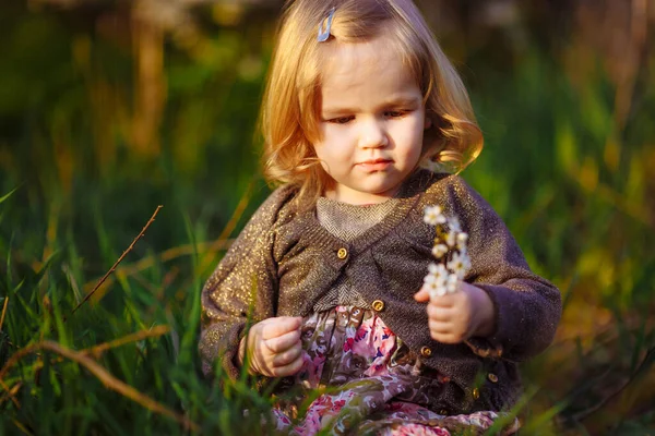 꽃핀 가지를 가진 어린 소녀가 풀에 앉아 있다 — 스톡 사진