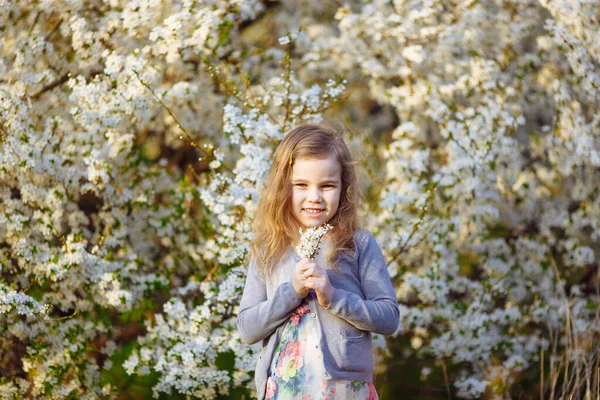 Kleines Mädchen in blühenden Büschen mit Zweig in den Händen. — Stockfoto