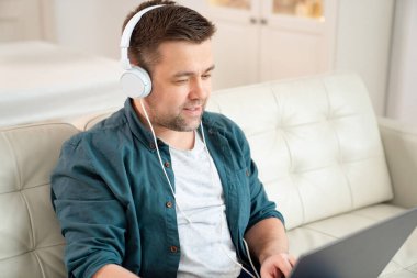 Öğrenci, müzik kulaklığı dinler. Koltuğa oturur.