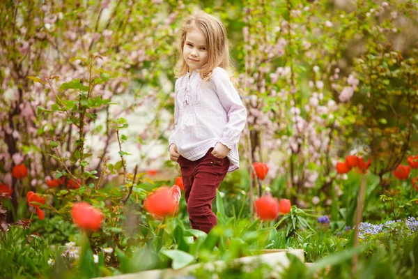 Menina pequena em canteiro de flores com amêndoa e tulipas — Fotografia de Stock