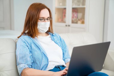 Tıbbi maskeli kadın çevrimiçi bilgisayarla çalışıyor.