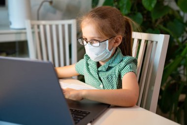 Gözlüklü ve maskeli çocuk bilgisayardan uzaktan kumanda öğreniyor.