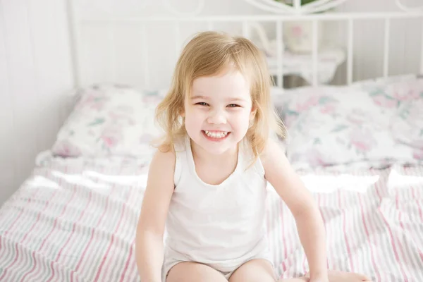 Criança menina ri sentado na cama no quarto dos pais . — Fotografia de Stock