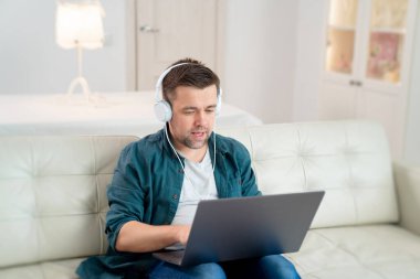 Serbest çalışan, müzik kulaklıkları dinleyen, kanepeye oturan.