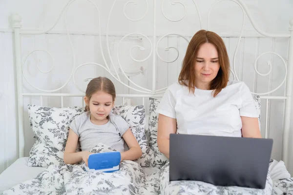 Stanna hemma flicka och mamma lära sig på datorn i sängen — Stockfoto