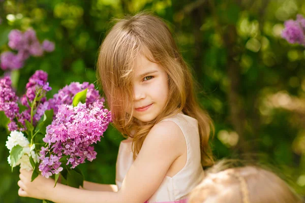一个小女孩站在开着花束的丁香花旁 — 图库照片