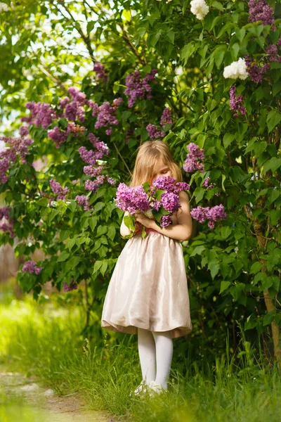 Niña en un vestido rosa cerca de una flor lila — Foto de Stock