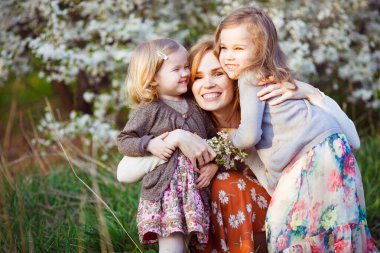 Anne ve kızları çiçekli çalılıklarda oturuyorlar. 