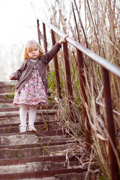 kid girl walks down stairs with high handrail.