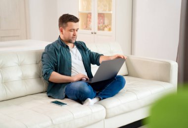 İnternette çalışan serbest çalışan adam kanepede oturuyor..