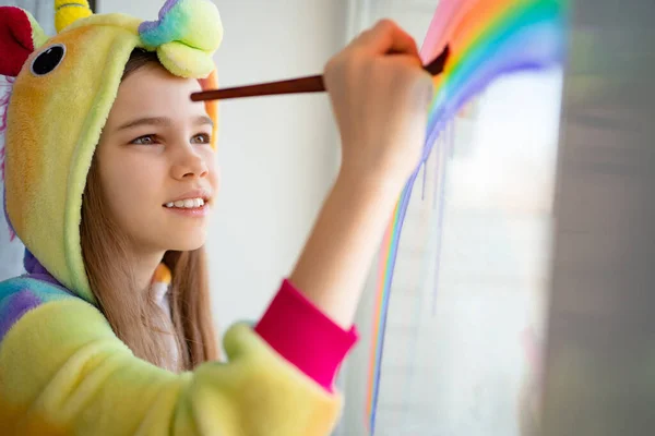 teen in kigurumi draws rainbow on window home