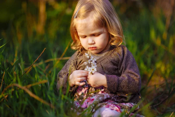 Niña sentada en la hierba con ramita en flor —  Fotos de Stock