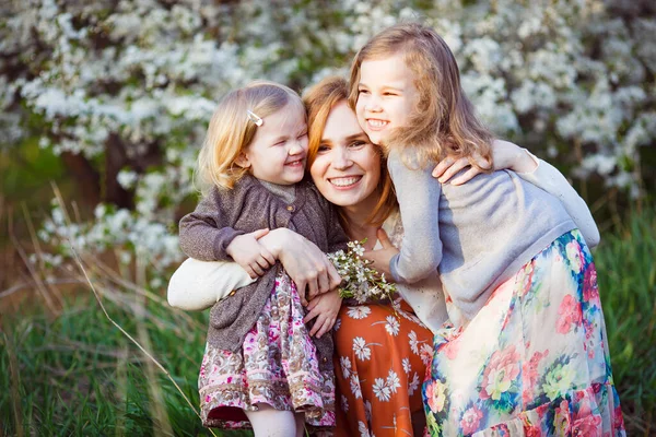 Mutter und zwei Töchter sitzen im blühenden Strauch — Stockfoto