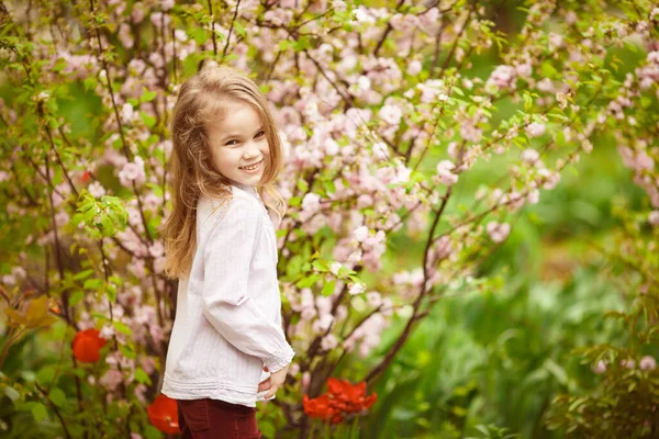 Menina criança no jardim com amêndoa arbusto e tulipas — Fotografia de Stock