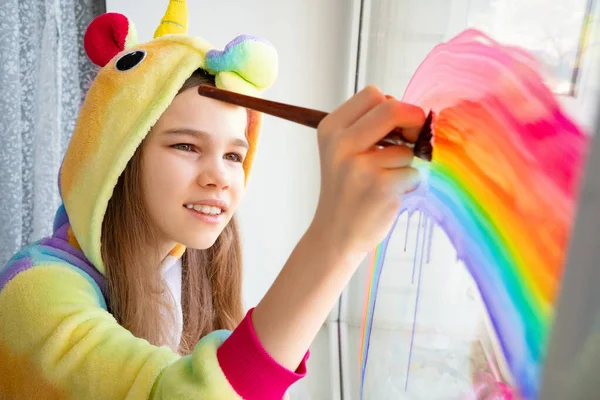 girl in kigurumi draws rainbow on window home