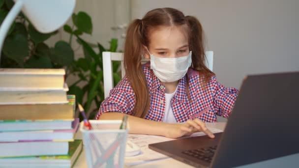 Uczennica w masce medycznej słucha lekcji na laptopie — Wideo stockowe