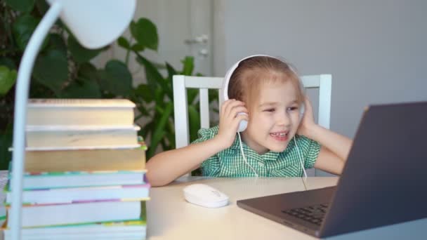 Маленька дівчинка в навушниках слухає музику на ноутбуці — стокове відео
