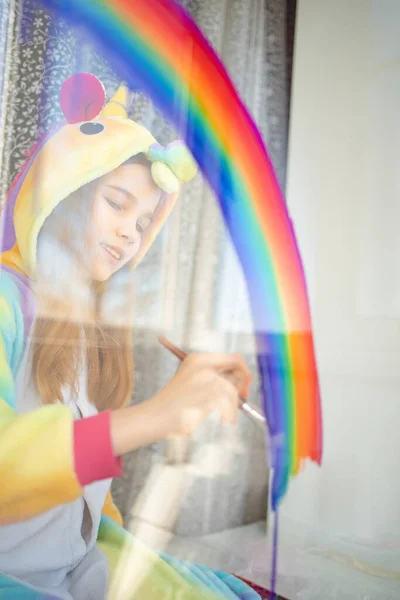 teen girl in kigurumi draws rainbow on window.