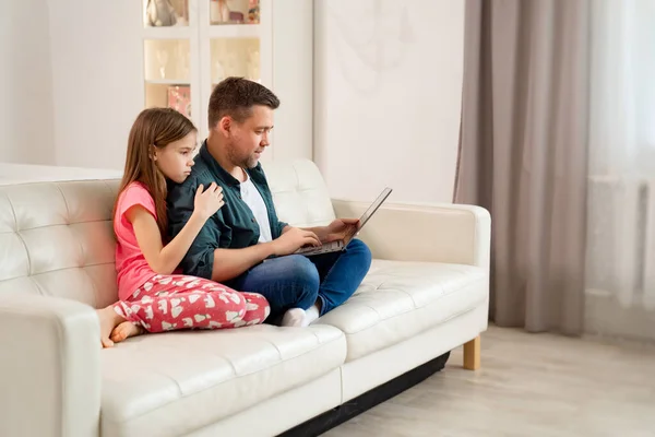Papá y niña trabajan en línea en el cuaderno en el sofá . — Foto de Stock