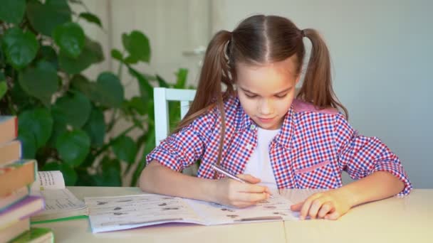 Школьница в клетчатой рубашке делает домашнее задание — стоковое видео