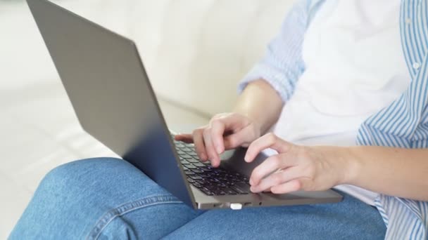 Жінка використовує ноутбук, вводить текст, сидить на дивані . — стокове відео