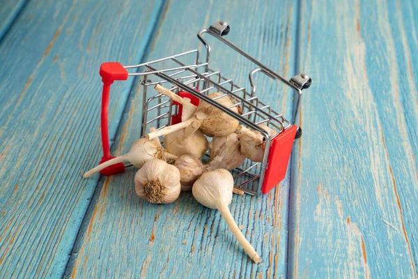 Kereta belanja mini biru bawang putih penuh di punggung kayu — Stok Foto