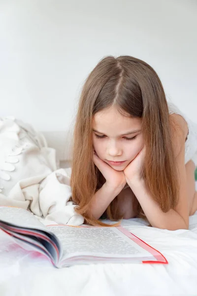 Концепція школи. маленька дівчинка з книгою лежить на ліжку — стокове фото