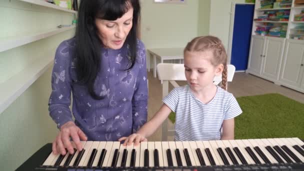 Teacher teaches kid girl to play on keyboard. — Stock Video