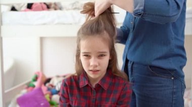 Anne küçük kızının kuyruğunu yapıyor.