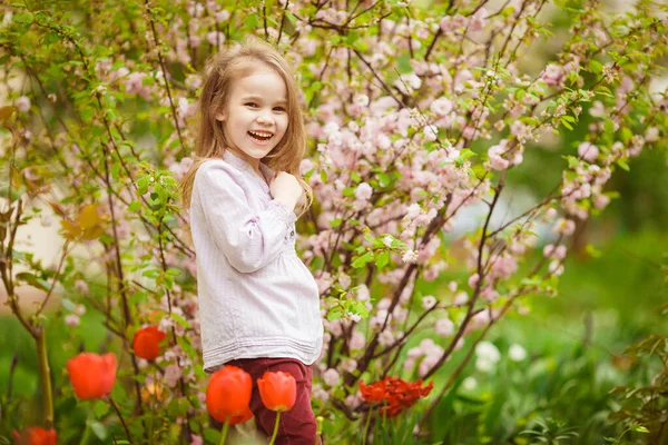 Drôle de petite fille près de avec amandier et tulipes — Photo