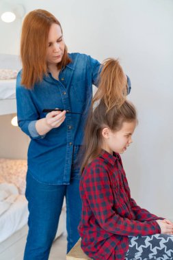 Anne küçük kızının kuyruğunu yapıyor. 