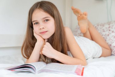 Okul konsepti. Kitaplı küçük kız yatağa uzanıyor.