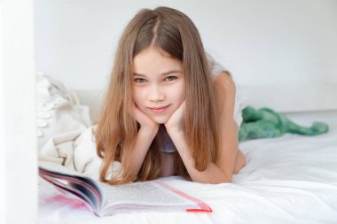Okul konsepti. Kitaplı küçük kız yatağa uzanıyor.