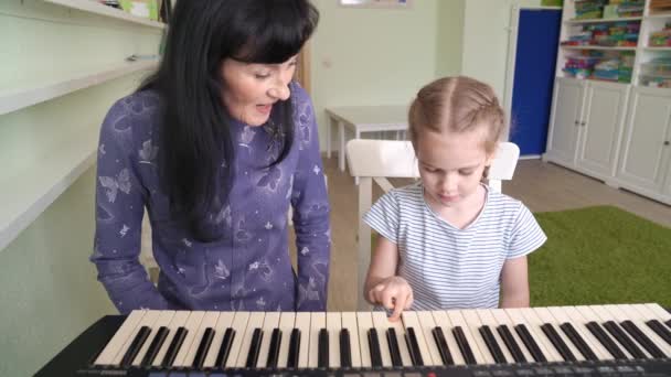 Nauczyciel uczy małą dziewczynkę grać na klawiaturze. — Wideo stockowe