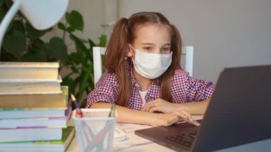 Sıhhiye maskeli kız laptoptan ders dinliyor.
